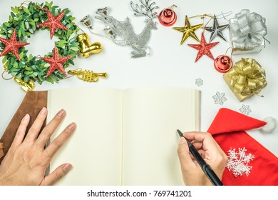 Christmas concept, Happy new year copy space and top view with silver reindeer, shiny gold silver and red blink star, christmas wreath, santa claus hat and gift box and hand on the notebook with pen.