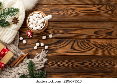 Christmas Concept. Top View Photo Of White Bobble Hat Plaid Cup Of Cocoa With Marshmallow On Rattan Placemat Giftbox Pine Branches Decorative Clip And Cinnamon On Wooden Desk Background With Copyspace