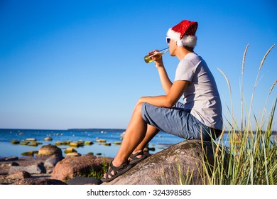 Christmas Concept - Young Handsome Man In Santa Hat Drinking Beer On The Beach