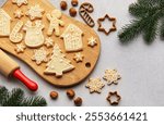 Christmas cookies decorated with icing displayed on a wooden board, along with fir branches and hazelnuts, creating a festive holiday scene