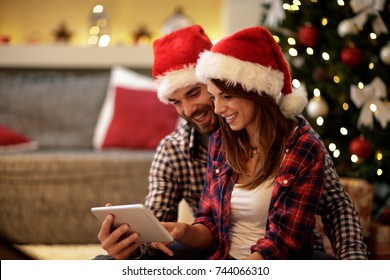 Christmas couple celebrating holiday and looking on tablet - Powered by Shutterstock