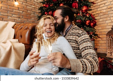 Christmas. Couple. Home. Togetherness. Man And Woman Are Drinking Champagne, Hugging And Laughing Near The Christmas Tree