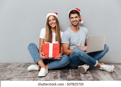 Christmas Couple With Laptop And Gift. Smiling. Gray Background