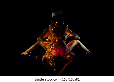 Christmas Couple In Love Of Sexy Man And Woman In Illuminated Garland And Santa Claus Hat Kiss On Black Background, New Year And Sex Games, Love