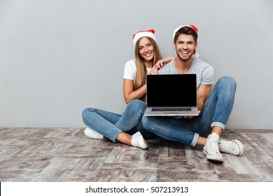 Christmas Couple Showing Laptop. Sitting Down. Gray Background