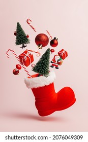 Christmas creative composition made with Santa Claus boot and flying pine tree, gift boxes and candy cane on pastel pink background. Minimal New Year shopping season concept. Winter holidays idea.	