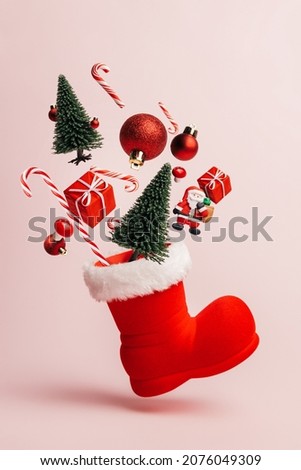 Christmas creative composition made with Santa Claus boot and flying pine tree, gift boxes and candy cane on pastel pink background. Minimal New Year shopping season concept. Winter holidays idea.	