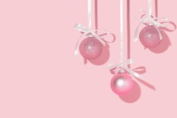 Christmas Creative Layout With Pink Christmas Baubles Hanging On Satin Ribbons On Pastel Pink Background. 80s Or 90s Retro Fashion Aesthetic Concept. Minimal New Year Idea With Copy Space.