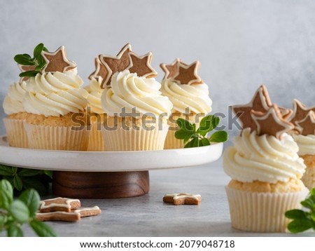 Christmas cupcakes on cakestand. Gingerbread cupcakes decorated with cream cheese frosting (whipped cream), gingerbread cookies and green leaves. New year and winter background. Close up food.