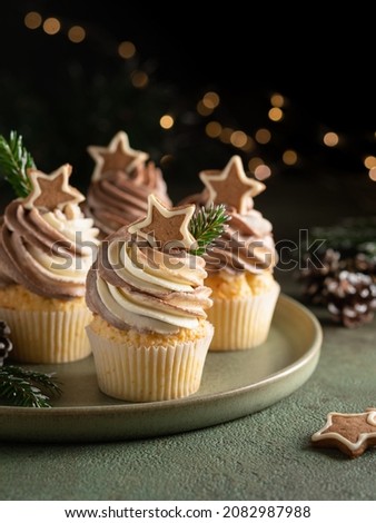 Christmas cupcakes on green ceramic plate. Gingerbread cupcakes decorated with cream cheese frosting (whipped cream) and gingerbread cookies. New year and winter background, xmas lights. 