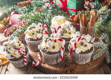 Christmas cupcakes. Xmas hot chocolate cupcake with peppermint candy cane, chocolate drops and marshmallow. Wooden background with Christmas decor and fir tree branches. Sweet Christmas baking - Powered by Shutterstock