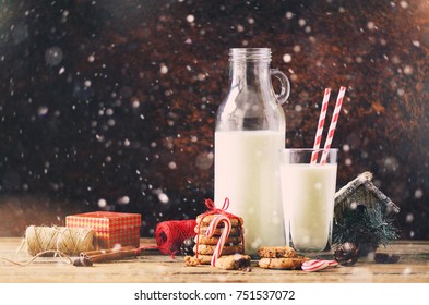 Christmas dark background with snow and bokeh, copy space. Bottle, glass with milk for Santa cookies red rope. anise stars, cinnamon sticks, cones, decor on wooden vintage table - Powered by Shutterstock