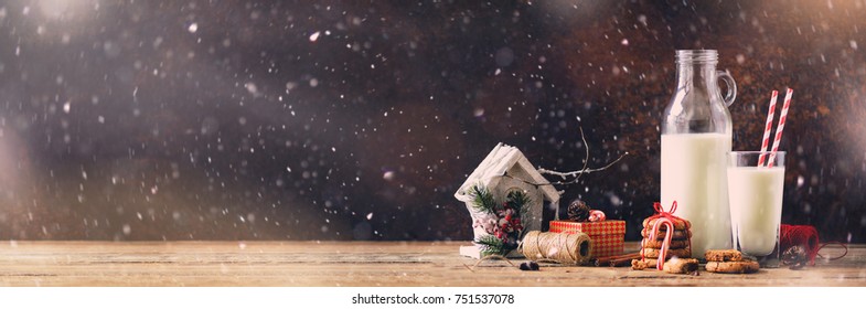 Christmas dark background with snow and bokeh, copy space. Banner. Bottle, glass with milk for Santa.cookies, red rope, anise stars, cinnamon sticks, cones, decor on wooden vintage table - Powered by Shutterstock