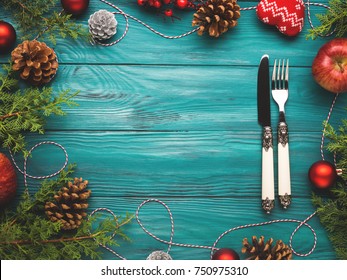 Christmas Dark Green Frame Background With Pine Cones, Red Baubles And Twine. Fork And Knife On Wooden Table Texture. Festive Holiday Dinner