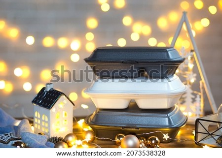 Christmas decor of food delivery service containers. New year's eve promotion. Ready-made hot order, disposable plastic box in fairy light. Work on public holidays catering. Copy space, mock up