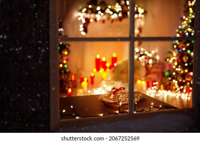 Christmas Decorated Room Interior With Garland Lights, Candles And Fir Tree. Winter Frosted Window Frame. Xmas Holiday Gingerbread Cookies For Santa At Table