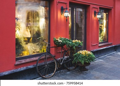 Christmas decorated showcase with old bicycle, fir branches, glass shiny toys and vintage lantern. Red building facade