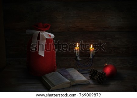 Christmas decoration with 2 Christmas candles, book, pine cones, red ball and Santa sack. Low-key lighting. Wooden background