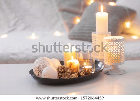 Christmas decoration   with burning candles on  white table against the background of  sofa with plaids and pillows. Cozy home and holiday concept