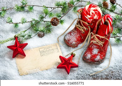 Christmas decoration red stars, sweets and antique baby shoes on snow background. Empty postcard for your text