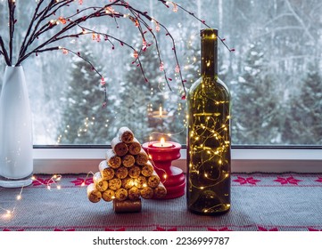 Christmas decoration set with wine bottle filled with micro led party lights and spruce tree made with used wine corks, behind is window with snowy countryside forest.  - Powered by Shutterstock