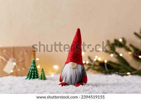 christmas, decoration and winter holidays concept - close up of gnome toy, gift box and fir trees made of green paper on artificial snow on beige background