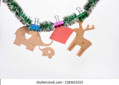 Christmas decorations concept. Wooden deer and elephant with paper for note hang on tinsel on white background. Decorations for Christmas holidays made out of natural materials and tinsel.