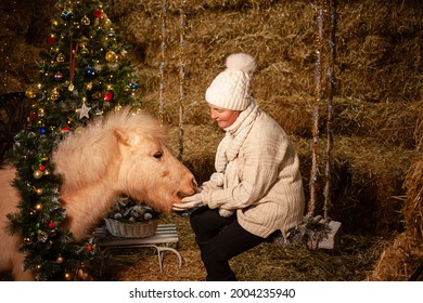 Christmas Decorations On The Stables. A Beautiful Pony With A Wreath Around His Neck. Christmas Tree With Balloons, Photo Zone For The New Year. The Older Woman Sits On The Swing