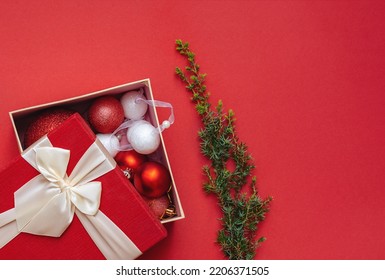 Christmas Decorations In Open Gift Box And Green Christmas Tree Branch Or Juniper On Plain Background. Red Packaging Lid With Lush Bow. Merry Christmas And Happy New Year. Copy Space.