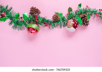 Christmas decorative red balls painted with white snow, green pine tree & cone, white curved circle lines & green big line on pink background and space with green white shiny decoration for xmas tree
