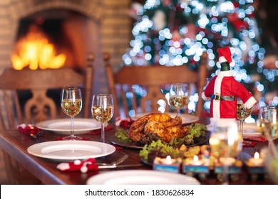 Christmas Dinner At Fireplace And Decorated Xmas Tree. Dish With Roasted Turkey, Salad And Baked Potato Served For Festive Family Meal. Wine Bottle With Santa Hat. Open Fire In Stone Oven.