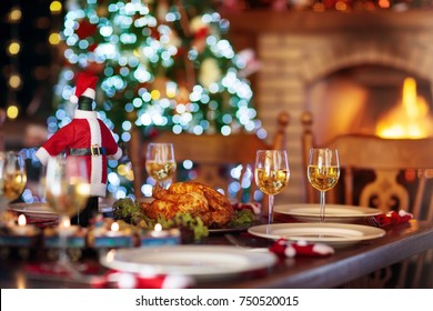Christmas dinner at fireplace and decorated Xmas tree. Dish with roasted turkey, salad and baked potato served for festive family meal. Wine bottle with Santa hat. Open fire in stone oven.