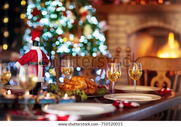 暖炉でのクリスマスディナーと クリスマスツリーの飾り付け 七面鳥の焼き物 サラダ 焼きポテトを添えた料理がお祝いの家族食事に出されます サンタハットのワインボトル 石のオーブンで火を焚きなさい の写真素材 今すぐ編集