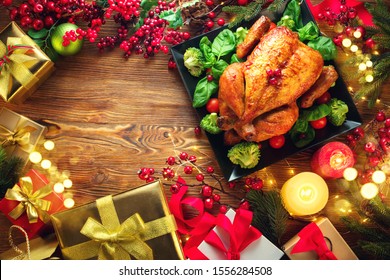 Christmas Dinner. Roasted Chicken. Winter Holiday Table Served, Decorated With Candles And Xmas Baubles. Roast Turkey Over Wooden Background With Christmas Tree, Table Setting Family Dinner With Gifts