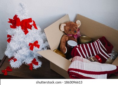 Christmas Donation Hampers, Help Refugees And Homeless. Xmas Charity Donation Box With Warm Clothes, Food And Toys Near Christmas Tree At Home. Charities Giving Christmas Hampers To Families In Need