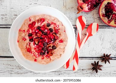 Christmas Eggnog Oatmeal With Crushed Candy Cane, Pomegranates And Chocolate Chips. Overhead View Table Scene On A Rustic White Wood Background.