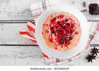 Christmas Eggnog Oatmeal With Crushed Candy Cane, Pomegranates And Chocolate Chips. Top View Table Scene On A Rustic White Wood Background.