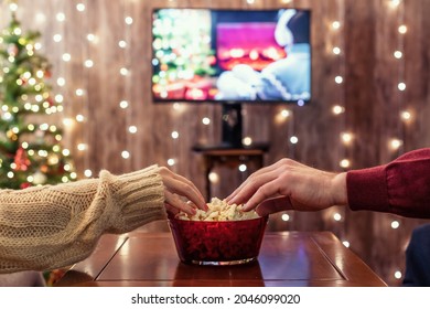 Christmas eve. Couple watching tv and eating popcorn. Home cinema. Cropped, close up 