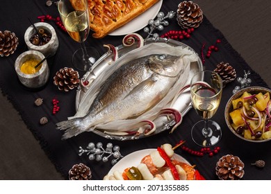 Christmas Eve Dinner. Baked Dorado Fish, Potato Salad, Fish Pie, Seafood Skewers. White Wine Glases. Festive Decoration. Feast Tradition. Dark Tablecloth.