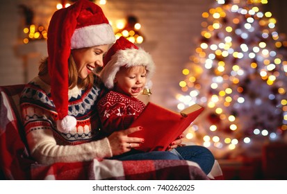 Christmas Eve. Family Mother And Baby Reading Magic Book At Home Near The Fireplace And The Christmas Tree
