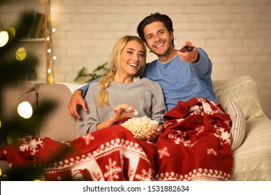 Christmas eve. Loving couple watching tv and eating popcorn at home, covered with blanket