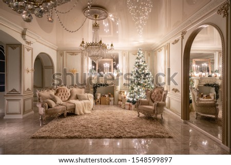 Christmas evening in the light of candles and garlands. Classic luxurious apartments with decorated christmas tree and presents. Living with fireplace, columns and stucco.