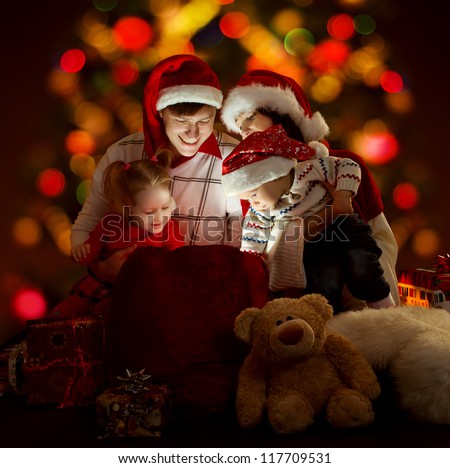 Christmas family of four persons in red hats opening lighting bag with gifts