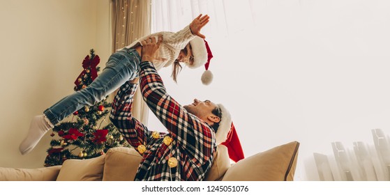 Christmas. Family. Fun. Dad Is Playing With His Little Daughter Near The Christmas Tree At Home. Both Are In Santa Hats