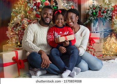 Christmas Family Portrait. Happy African American Father, Mother And Daughter Posing Near Xmas Tree In Decorated Living Room