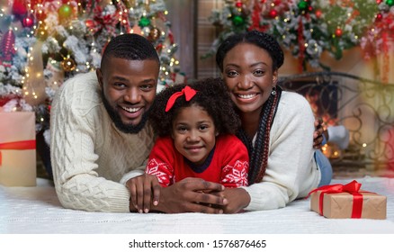 Christmas Family Portrait Near Xmas Tree At Home. Black Father, Mother And Their Little Daughter Celebrating Winter Holidays Together