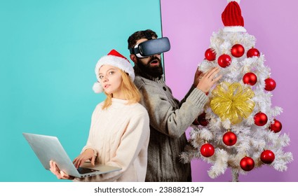 Christmas family using VR glasses and laptop. Bearded man in virtual reality goggles headset. Woman in Santa hat with notebook. Christmas couple near Christmas tree. Winter holidays and entertainment. - Powered by Shutterstock