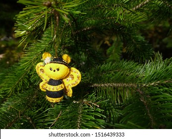 Christmas felt decoration on a spruce branch. Handmade bauble figurines a cute bee. Holiday background with a copy space. Suitable for greeting cards, banners and posters.