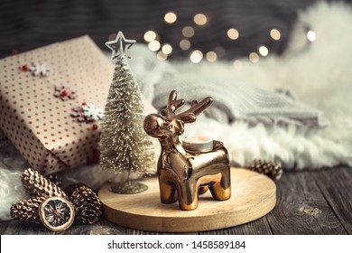 Christmas festive background with toy deer with a gift box, blurred background with golden lights, festive background on wooden deck table and cozy sweater on background