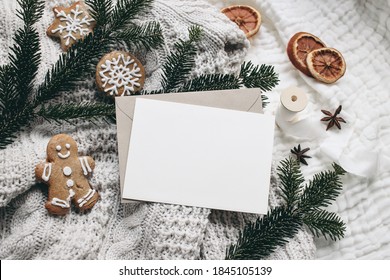 Christmas festive still life. Blank greeting card, invitation mockup and envelope  on knitted sweater . Gingerbread cookies, dry oranges and fir branches on wool blanket. Selective focus, top view.  - Powered by Shutterstock